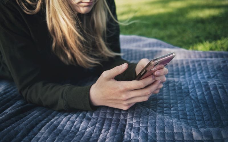Chatpartner. Mädchen liegt mit Smartphone im Gras